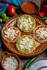 Mexican picaditas with sauce and fresh cheese on wooden background