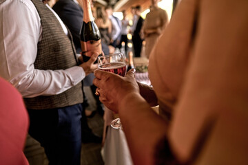 Bartender pouring champagne into glasses. A lot of people and a woman are standing with a glass of champagne. Focus on the glass.