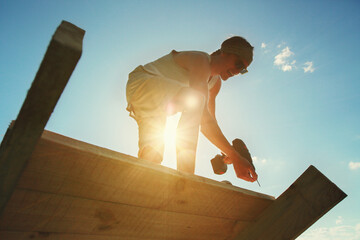 Young Caucasian man drills wood at sunset with a screwdriver. - obrazy, fototapety, plakaty
