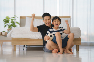 excited father and son cheering and watching sports match in bedroom