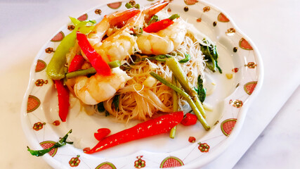 Stir-fried rice vermicelli with water mimosa and prawns in white dish or plate at Chinese restaurant. Close up Thai spicy food on white table. 