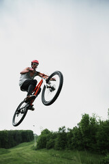 Young Caucasian man jumping on a mountain bike from a springboard in the forest.