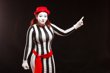 Portrait of female mime artist performing, isolated on black background. Woman in a striped dress...