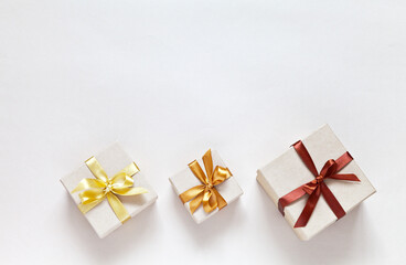 Three gift boxes with satin bows on a light background. Ecological packaging in kraft paper. Festive delivery of goods. Surprises for a family celebration. Flat lay, copy space, mock up, greeting card