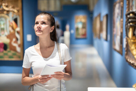 Portrait of young female visitor with paper guide at paintings exposition