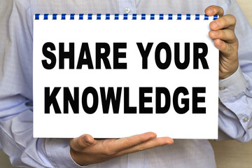 The businessman shows a sheet with the text OF share your KNOWLEDGE on a white background. Business concept