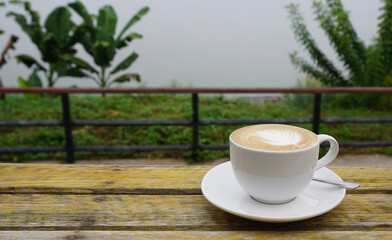 Hot latte coffee with leaf art in white cup on rustic timber table