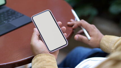 Male hand holding smartphone while working with tablet on coffee table