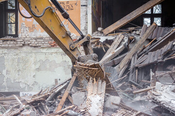 Demolition of an old brick building with an excavator bucket
