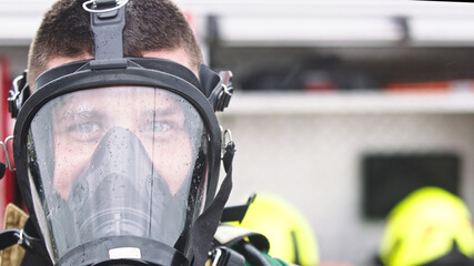 Close up, portrait of firefighter wearing gas mask in front of the burning house. High quality photo