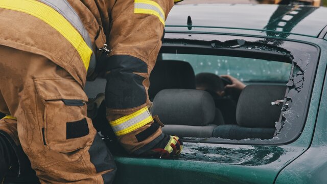 Firefighter beraking glass on car window extricate trapped victim from the car. High quality photo