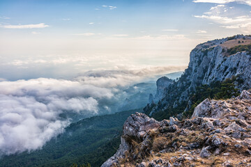 A majestic view of the rocky mountains and the valley in fog and clouds. Creamy fog covered the mountain valley in sunset light. Picturesque and gorgeous scene. Misty sunset over Crimea Mountains