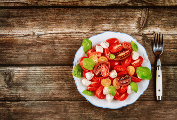 Tasty salad made from cherry tomato, mozzarella cheese and basil on white plate with fork.