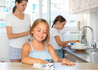 Obraz premium Two little daughters help mom clean the kitchen at home