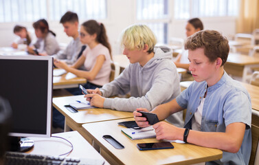 Obraz na płótnie Canvas Portrait of teen pupils using mobile phones during lesson