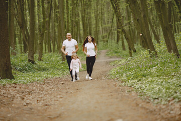 Fototapeta premium Family in a summer forest. Woman and man in a white t-shirts. Daughter with parents.