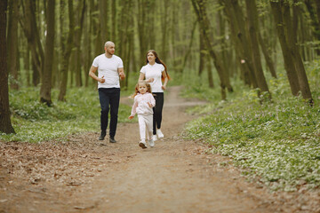 Fototapeta premium Family in a summer forest. Woman and man in a white t-shirts. Daughter with parents.