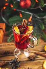 Cup of aromatic hot mulled wine on a wooden table on the background of a Christmas tree with lights. Concept of a festive atmosphere