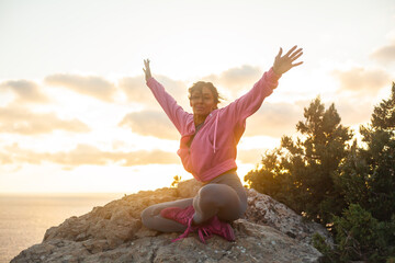 Woman sitting on a mountain top admires the beautiful rising sun over the sea or ocen and enjoys...