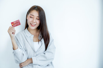 Naklejka premium Portrait of a lovely young Asian beautiful woman with long hair holding a red credit card, her eyes sparklingly at the camera. Ready to pay shopping according to discounted products