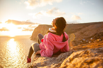 Back view of woman sitting on a mountain top admires the  rising sun over the sea or ocean and enjoys the beautiful view. Meditations are beneficial outdoors in solitude from the bustle of the city