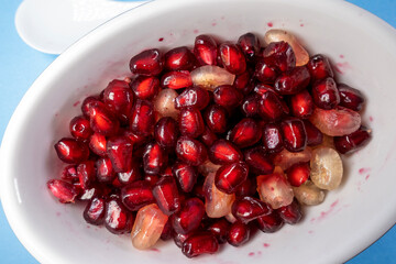 Fresh pomegranate seeds on plate with blue background