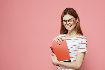 female student with notepads on pink background gesturing with her hands glasses on her face striped t-shirt model