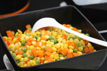 Corn, carrots and peas in a black bowl with white spoon