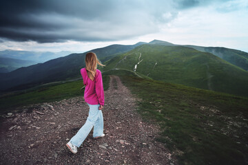 Fototapeta premium Young caucasian woman in a sweater traveling through the mountain peaks in cloudy weather.