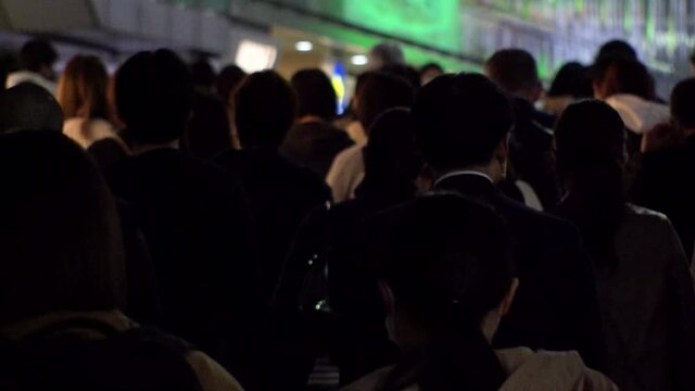 TOKYO, JAPAN : Crowd of people at the street in night time rush hour. Back shot of people walking to train station after work. Japanese city life style, business and work concept shot. Slow motion.