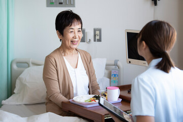 入院ベッドで看護師と話をする高齢女性