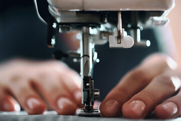 Close-up of woman seamstress hands behind a sewing machine indoors near the window. Close-up of a tailor near a sewing machine.