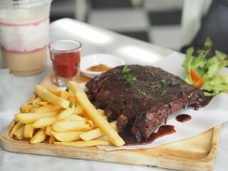 Pork Spareribs BBQ, Barbeque Pork Ribs with french fries vegetable salad, tomato sauce in a clear glass on wooden tray, food delicious