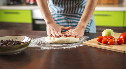 Female chef is kneading dough with her hands in the kitchen for making homemade pizza.