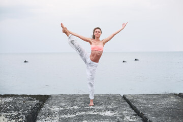Young caucasian woman doing yoga in sea water on the coast.