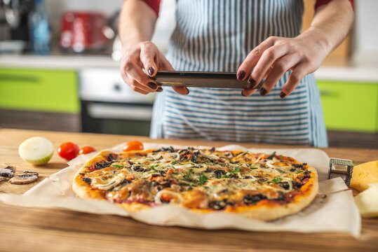 Female chef blogger takes photos of home-made pizza on her phone. The concept of food photography for social networks