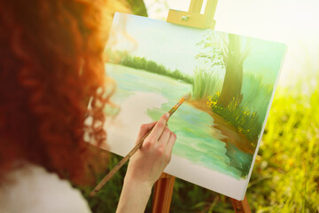Young caucasian woman painting on an easel in the forest at sunset.