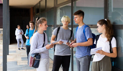 Group of positive teenagers resting outdoors in schoolyard during break in lessons. Back school concept .