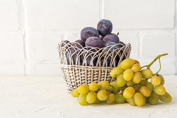 Just picked plums and grapes in wicker basket on white backdrop.