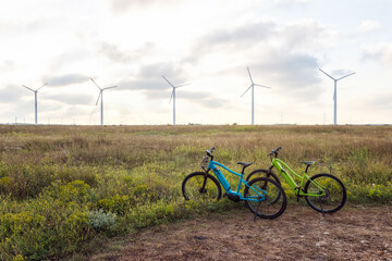 Fototapeta na wymiar Amazing view with electric bikes in a field against the backdrop of wind turbines. Green energy, sustainable alternative electricity, no pollution environment.