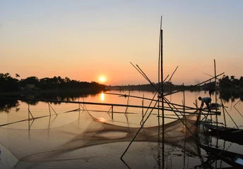 Tableau sur aluminium Paysages A man spread his net to catch fish and waiting , the sun is yellowish in color .  © Gunjan