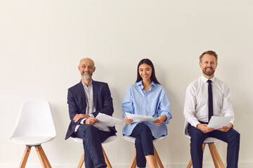 Three positive candidates of different ages sitting on chairs waiting for job interview
