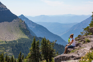 Woman sitting on the edge of scenic mountain overlook drinking water. Hiking up a Beautiful...