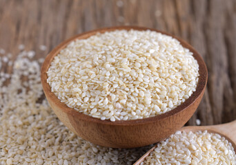 White sesame in a wooden bowl on a wooden background.