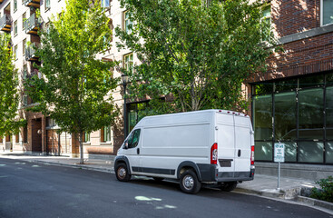 Compact industrial cargo mini van standing on the urban city street with multilevel apartments...
