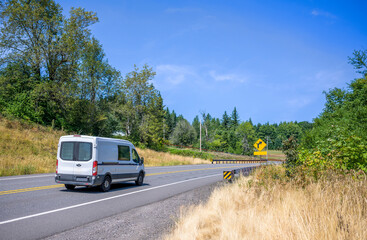 Compact white cargo mini van for small business purpose driving on the winding summer road with beautiful nature around