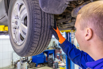 Close-up shot of mechanic checking very attentively surface of a car tire. Mechanic wearing blue coverall and orange gloves. Car is on a hydraulic lift