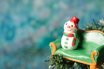 A snowman model sitting on a green sofa with a blurry bokeh background