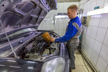 Car mechanic replacing and pouring oil into engine at car service station during regular check-up routine