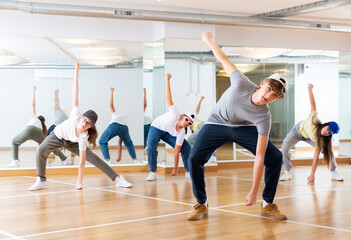 Fototapeta premium Positive teenage girls and boys training hip hop in dance studio, dance classes for teens